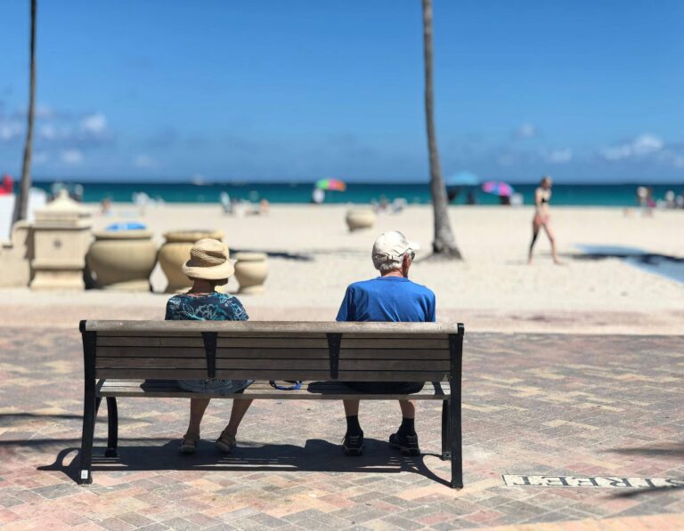 Two retirees with long-term Thailand visas sit on a bench overlooking a beach